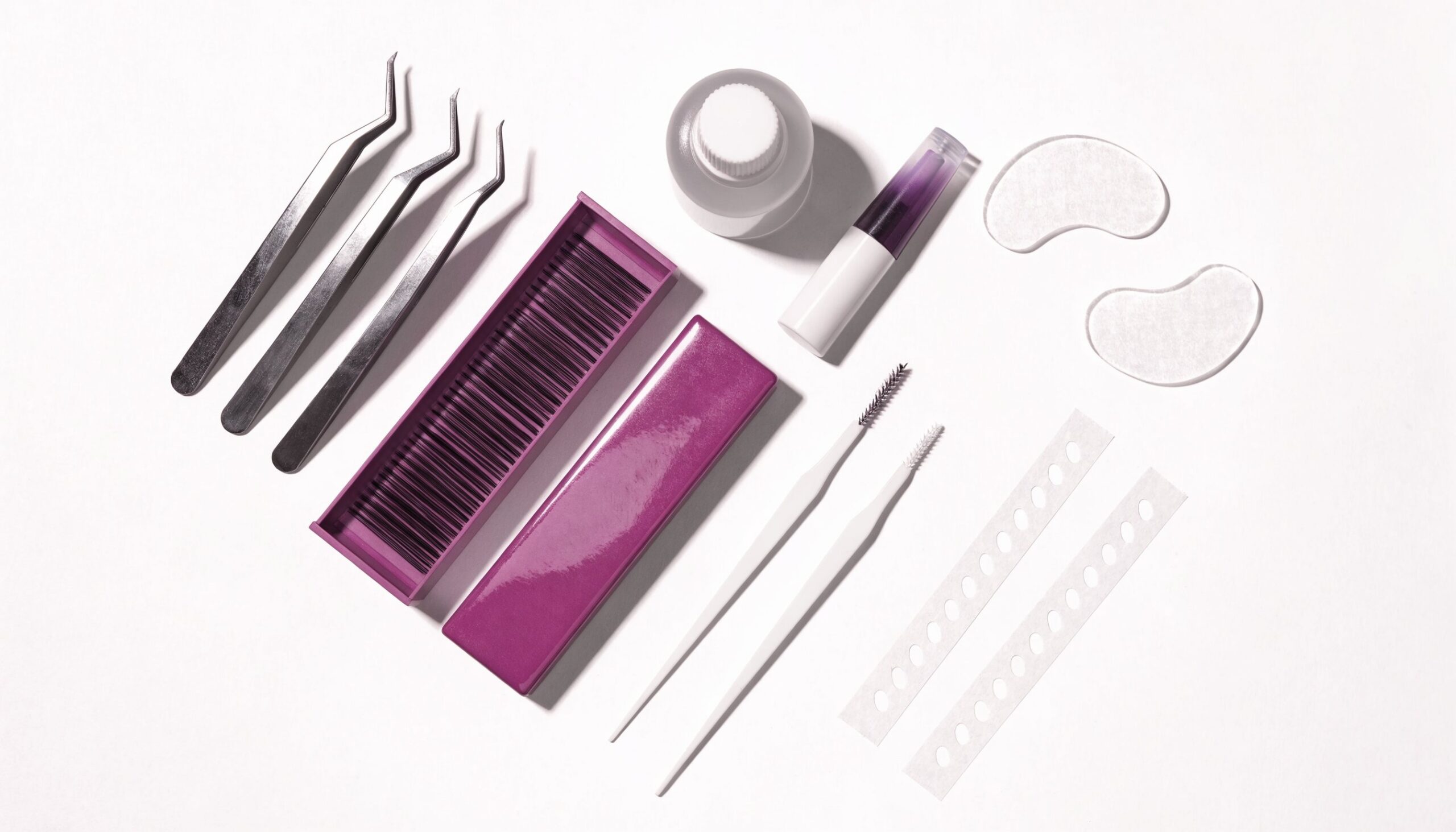Flatlay einer Wimpernverlängerung-Startausstattung mit Pinzetten, Trays, Kleber und Pads auf Weiß