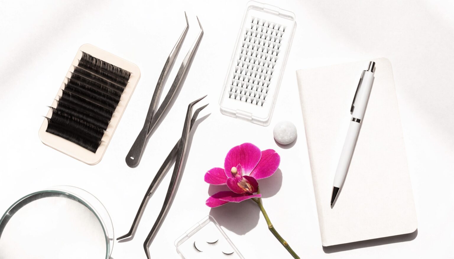 Helles weißes Flatlay für die Wimpernvolumen-Schulung: Lash-Tray, Volumen-Fächer, Pinzetten, Notizbuch und Magenta-Orchidee