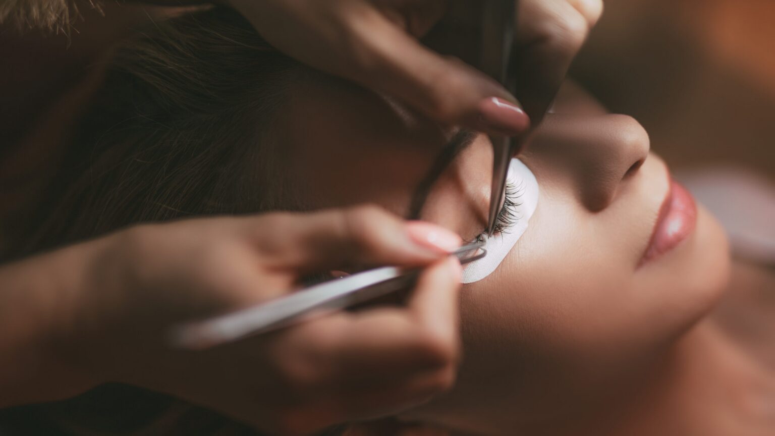 Arbeitsprobe Wimpernverlängerung: Stylistin setzt mit zwei Pinzetten Extensions am Modell