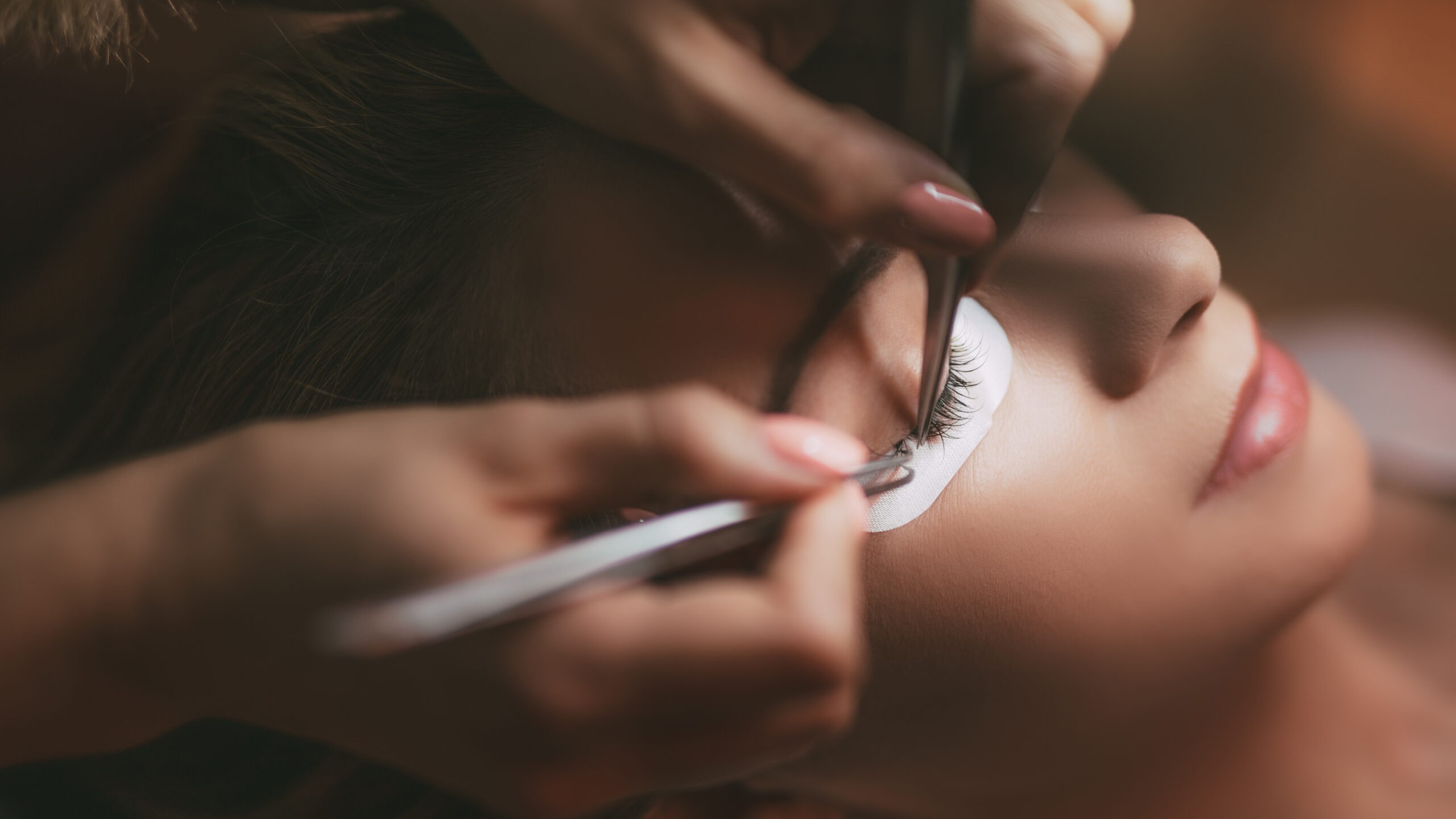 Arbeitsprobe Wimpernverlängerung: Stylistin setzt mit zwei Pinzetten Extensions am Modell