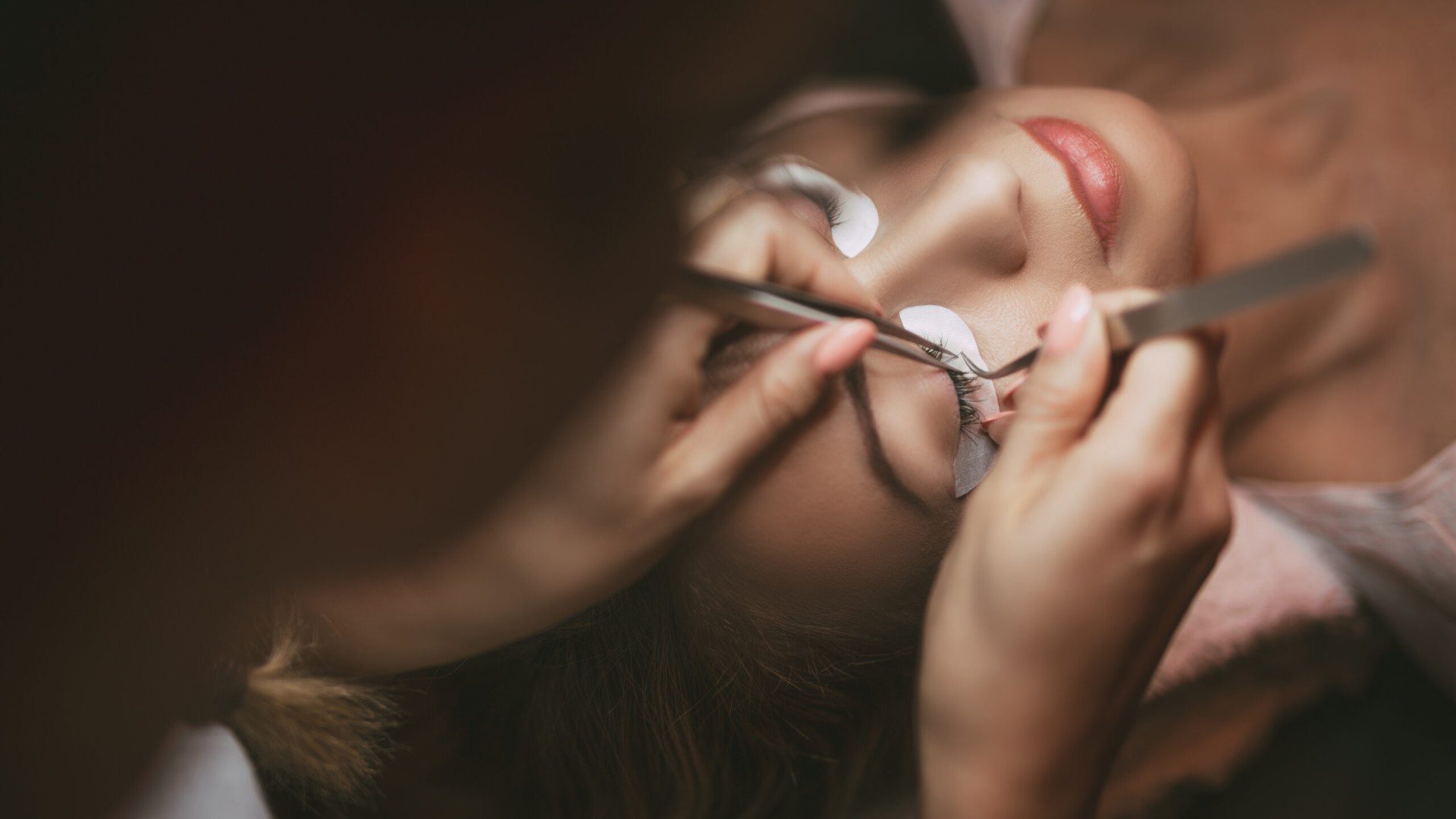 Wimpernverlängerung auffüllen: Stylistin setzt mit zwei Pinzetten neue Extensions beim Refill